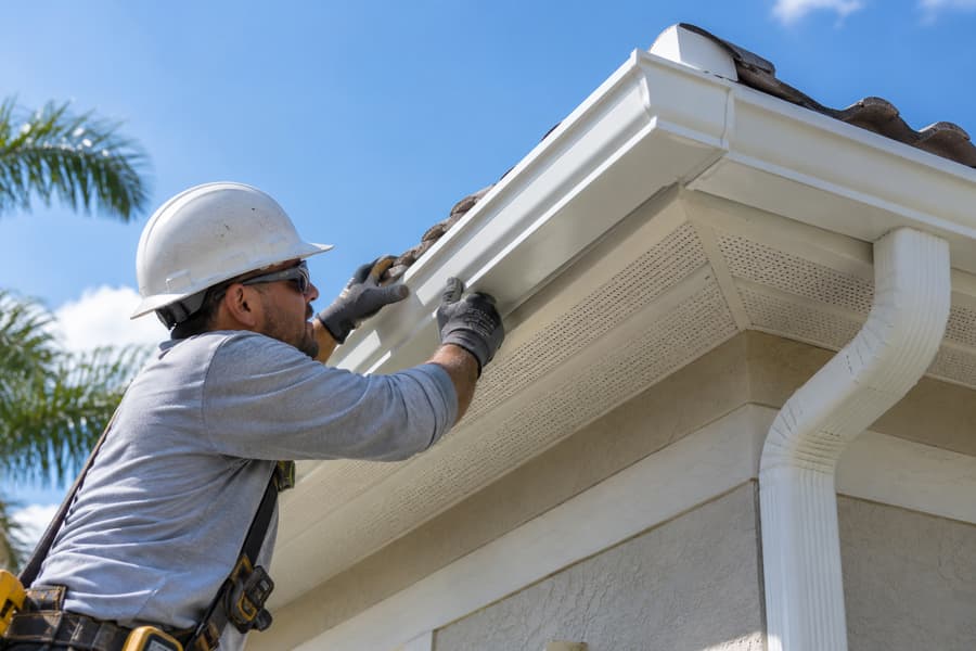 Technician in a hard hat installing a white seamless gutter on a Florida home